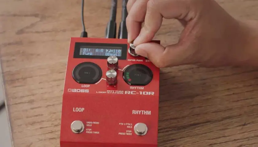 Dłoń kręci gałką na czerwonym looperze do gitary Boss RC-10R, ustawiając rytm funk.