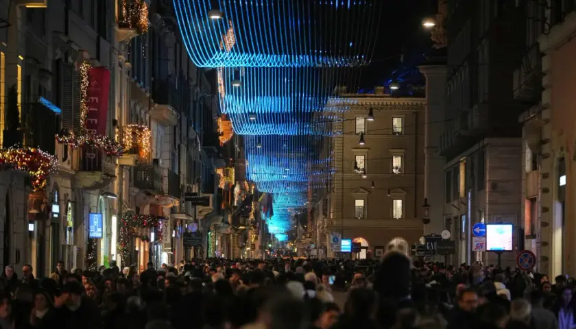 Folla festosa in strada a Roma, 25 dicembre, sotto luminarie blu e decorazioni natalizie.