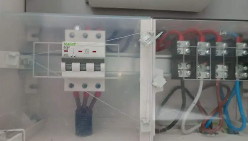 Trzybiegunowy wyłącznik nadprądowy w obudowie z przezroczystego plastiku, podłączony do przewodów.