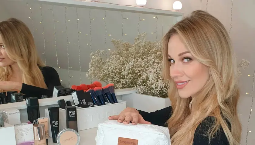 Blondynka z kosmetykami, szuka inspiracji, czym pomalować twarz na biało.