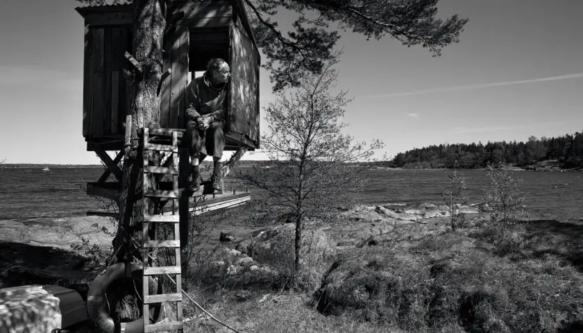 Man i trädkoja vid havet, som hämtad ur en berättelse av John Ajvide Lindqvist. Barnens lekplats blir en plats för eftertanke.