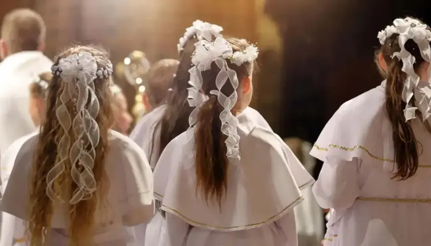 Dzieci w białych strojach, z wiankami na głowach, czekają na moment, kiedy jest komunia.