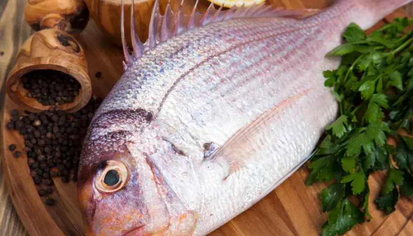Un pescado rojo, listo para cocinar con perejil, limón, sal y pimienta negra.