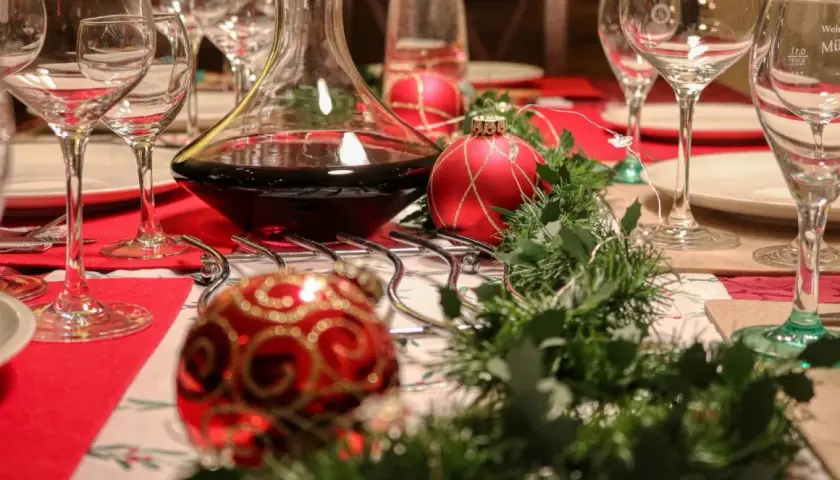 Table dressée pour Noël avec carafe de vin rouge. Combien de cubi de vin pour 40 personnes ? Boules rouges et guirlande verte.