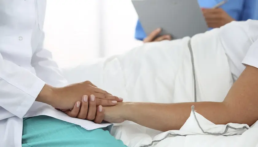 Lekarz uspokaja pacjenta, który leży w łóżku. W tle inny medyk notuje coś na kartce. Ustawa o niepełnosprawnych bez kolejki zapewnia im priorytet.
