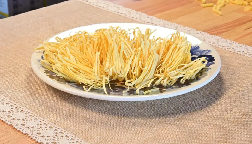 Talerz pełen cienkiego, żółtego makaronu pszennego, idealnego do przygotowania pysznego obiadu. Zastanawiasz się, ile makaron pszenny kcal ma porcja?