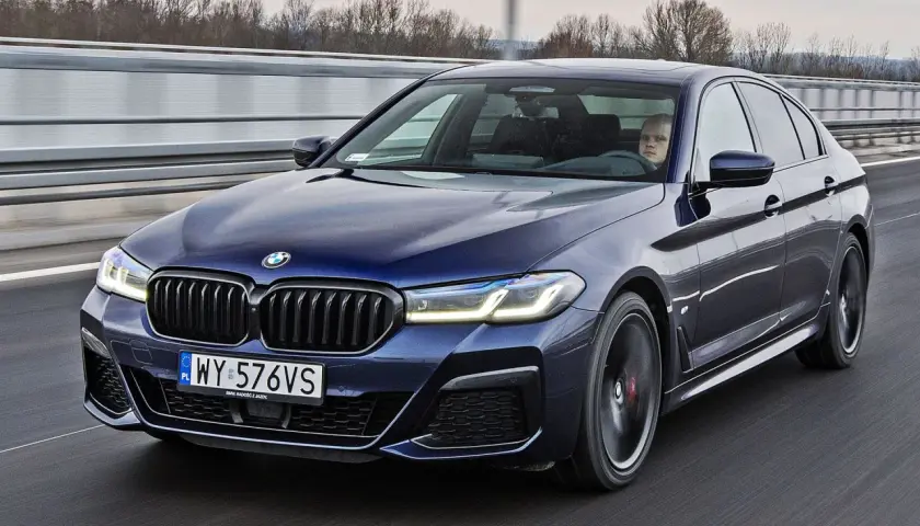 Ciemnoniebieskie BMW 520d xDrive jedzie autostradą. Kierowca z zaciekawieniem obserwuje drogę.