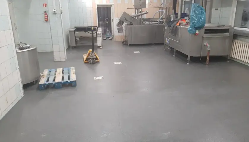Nowa, szara wylewka betonowa w kuchni przemysłowej schnie, czekając na dalsze prace.