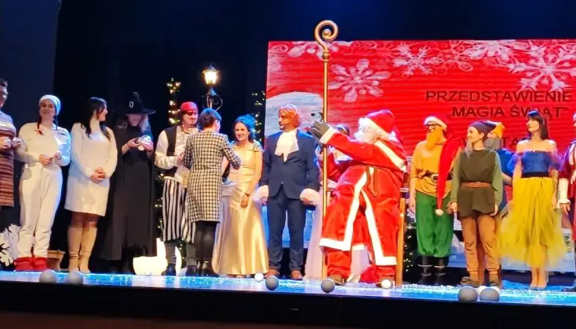 Aktorzy w strojach świątecznych i bajkowych na scenie, w tym Święty Mikołaj.