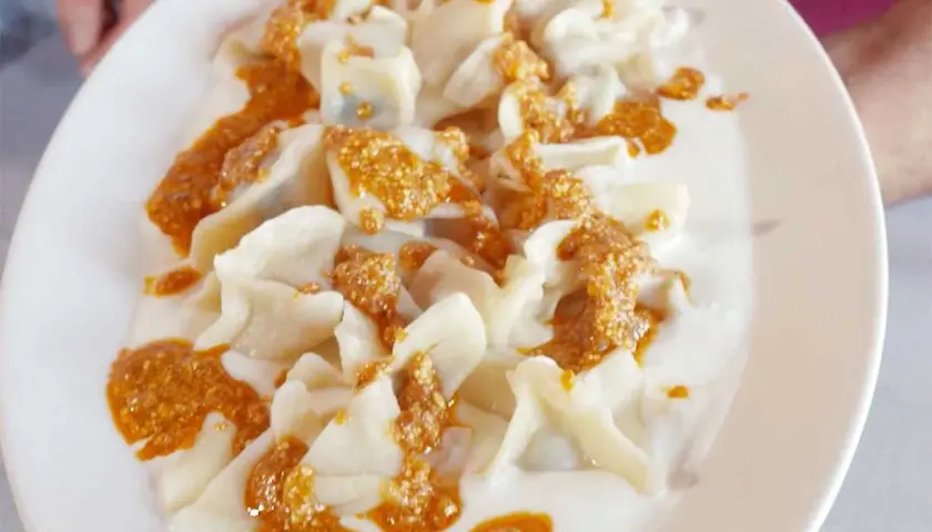 En tallrik med manti, små dumplings i en krämig sås med en kryddig topping. Perfekt för ett manti recept.