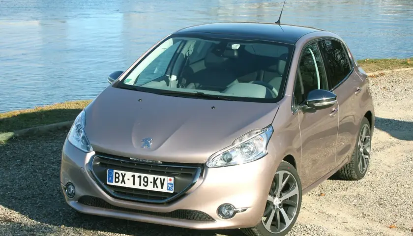 Peugeot 208 GPL color bronzo, parcheggiata su ghiaia vicino a un lago.