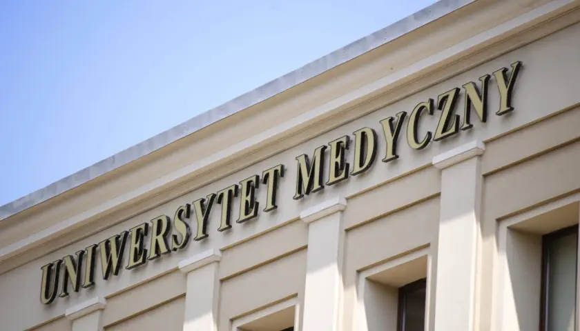 Napis "Uniwersytet Medyczny" na jasnej fasadzie budynku pod błękitnym niebem.
