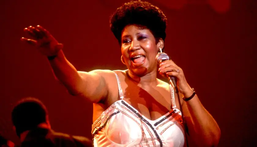 Aretha Franklin śpiewa na scenie, trzymając mikrofon. Jej dzieci z pewnością byłyby dumne z jej występu.