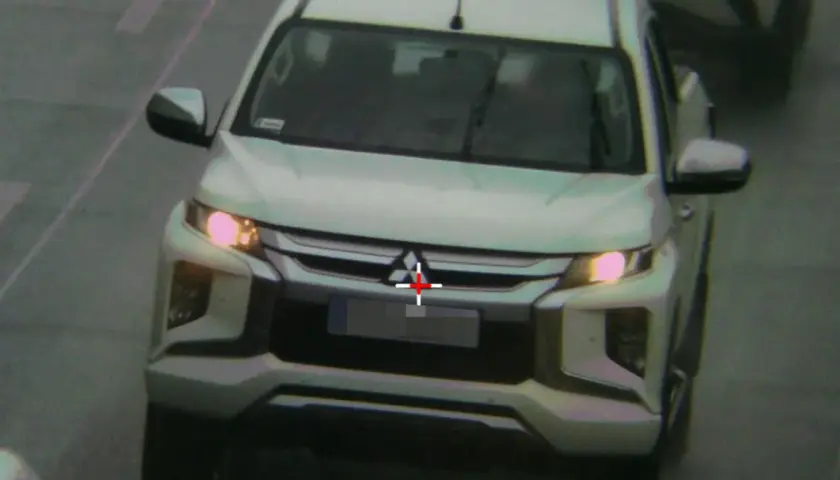 Biały pickup jedzie zderzakiem do przodu, z czerwonym krzyżem na grillu.
