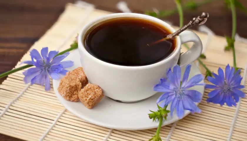 Aromatic kawa z cykorii, ozdobiona niebieskimi kwiatami i kostkami brązowego cukru, na bambusowej macie.
