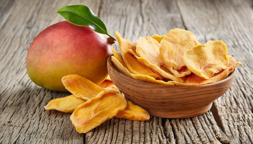 Un mango fresco e una ciotola di mango disidratato, che ne esaltano le proprietà nutritive e il sapore concentrato.