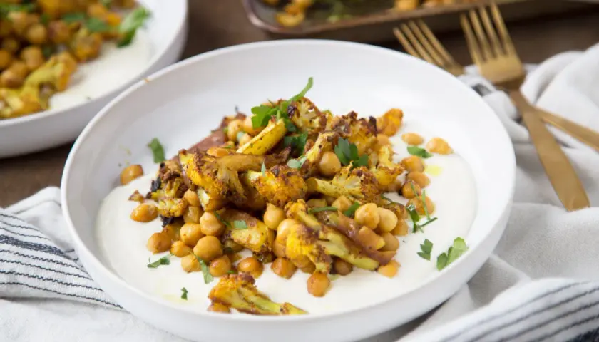 Chou-fleur rôti aux épices, pois chiches et sauce crémeuse. Un délice de chou fleur barbecue, garni de persil frais.