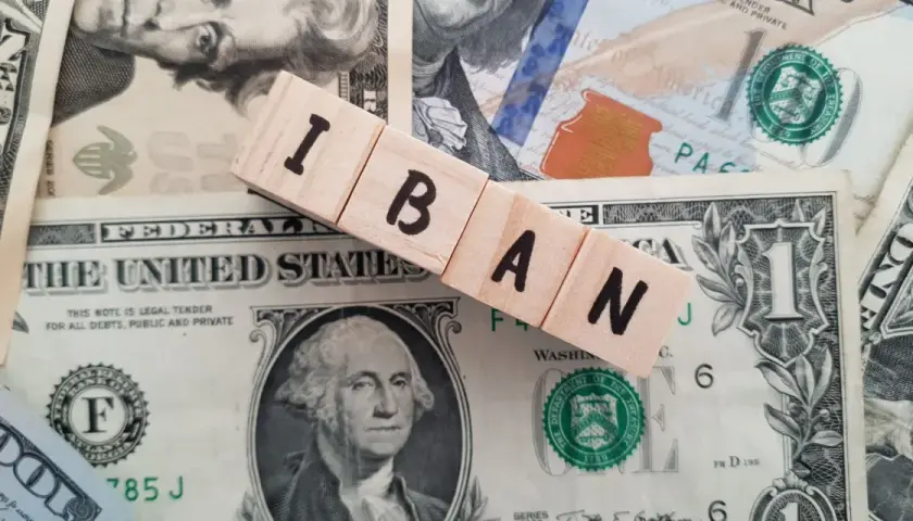 Drewniane klocki z literami IBAN leżą na banknotach dolarowych.