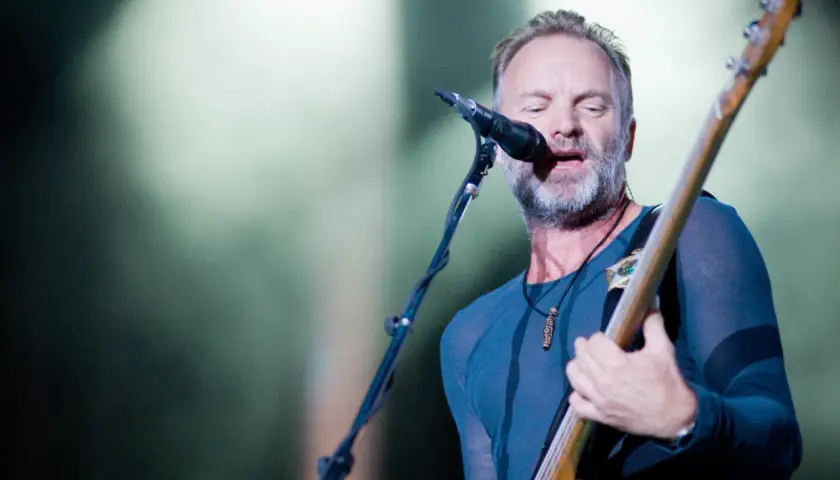 Sting, wokalista The Police, gra na gitarze basowej i śpiewa do mikrofonu na koncercie.