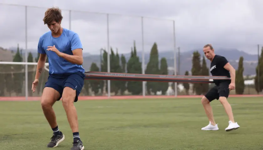 Zwei Männer trainieren auf einem Fußballfeld mit einem Widerstandsband für einen explosiven sprint.