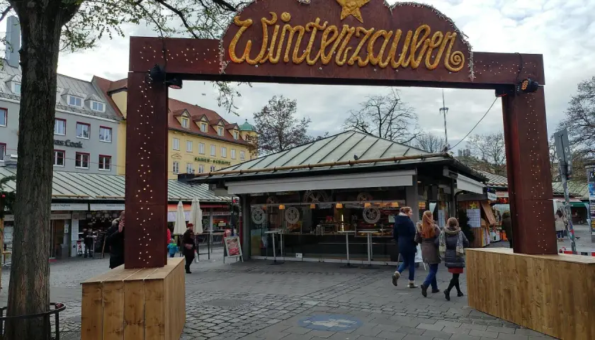 Der Viktualienmarkt zeigt seinen Winterzauber. Menschen schlendern vorbei an Ständen, die auf den Weihnachtsmarkt einstimmen.