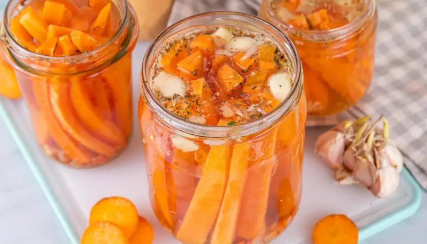Gläser mit karotten fermentieren, gefüllt mit Karottenstücken, Knoblauch und Kräutern. Ein ganzer Knoblauch liegt daneben.