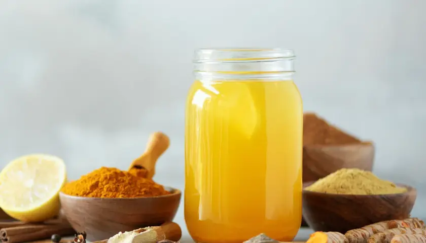 Ein Glas mit gelbem Getränk, daneben Schalen mit Kurkuma Pulver, Ingwer und Gewürzen. Perfekt zum Kurkuma Pulver trinken.