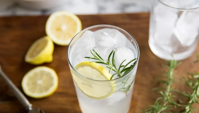 Orzeźwiający gin i tonic z plasterkiem cytryny i gałązką rozmarynu, otoczony świeżymi cytrynami.