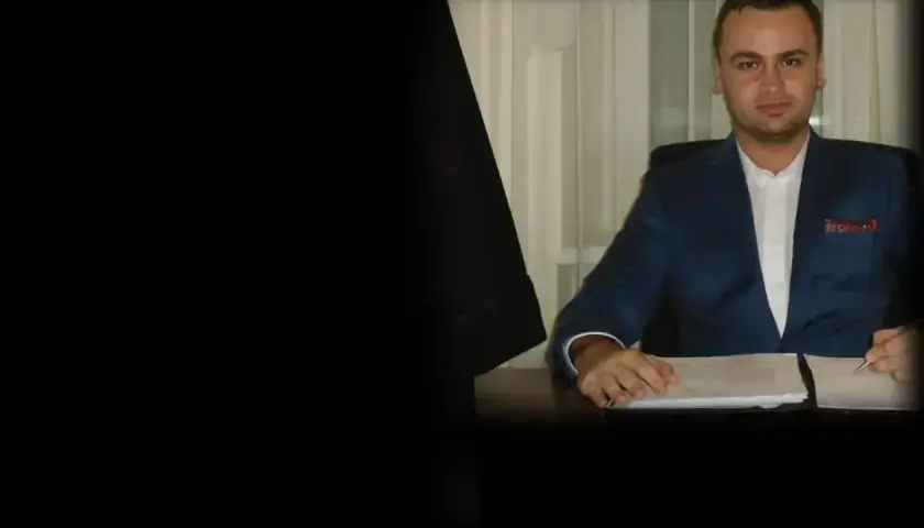 Mężczyzna w garniturze siedzi przy biurku z dokumentami.
