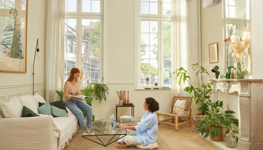 Dos mujeres disfrutan de un ambiente confortable en un salón luminoso, con el aire acondicionado en modo quiet funcionando discretamente.