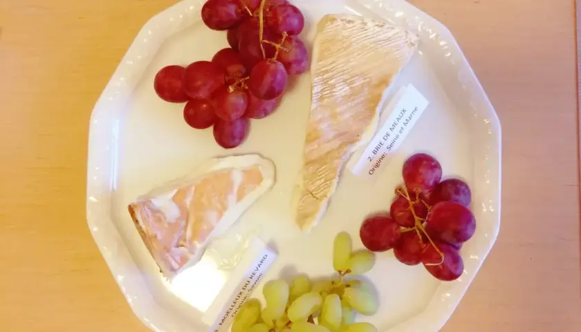 Talerz z serami Brie de Meaux i Moelleux du Revard, winogronami i etykietami, idealny do degustacji kuchni francuskiej.