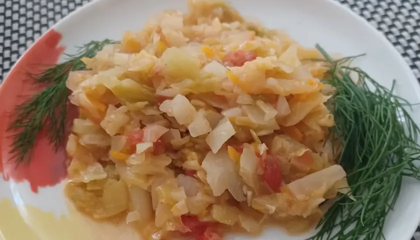 Młoda kapusta z pomidorami, duszona z koperkiem, na białym talerzu.