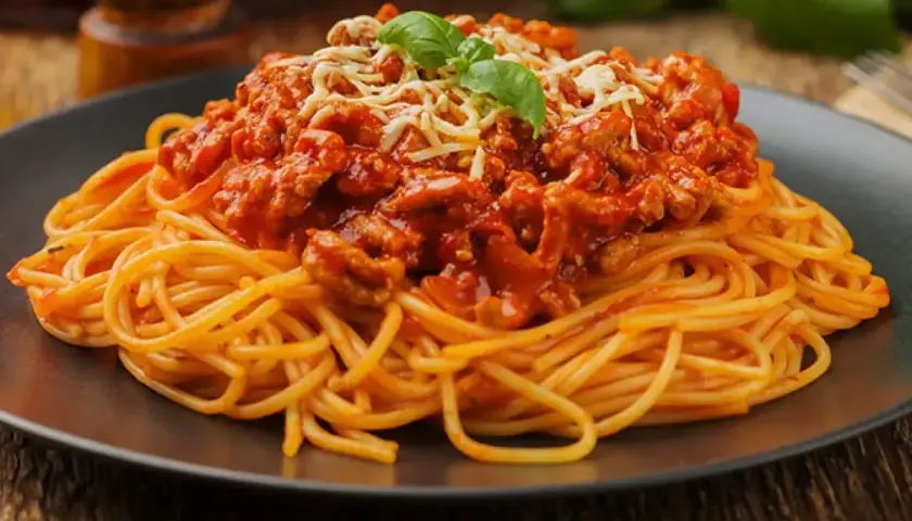 Porcja spaghetti z bogatym, mięsnym sosem bolognese, posypana startym serem i listkiem bazylii.