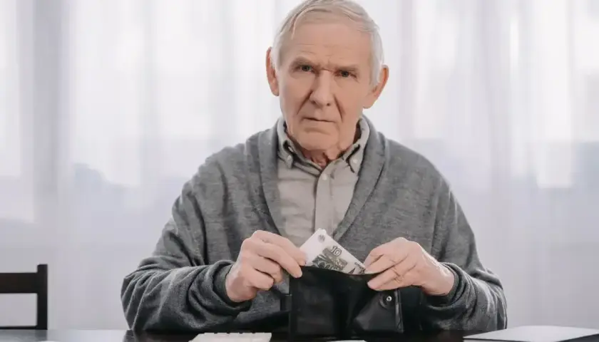 Zmartwiony senior wkłada pieniądze do portfela, planując kiedy na wcześniejszą emeryturę po nowemu.