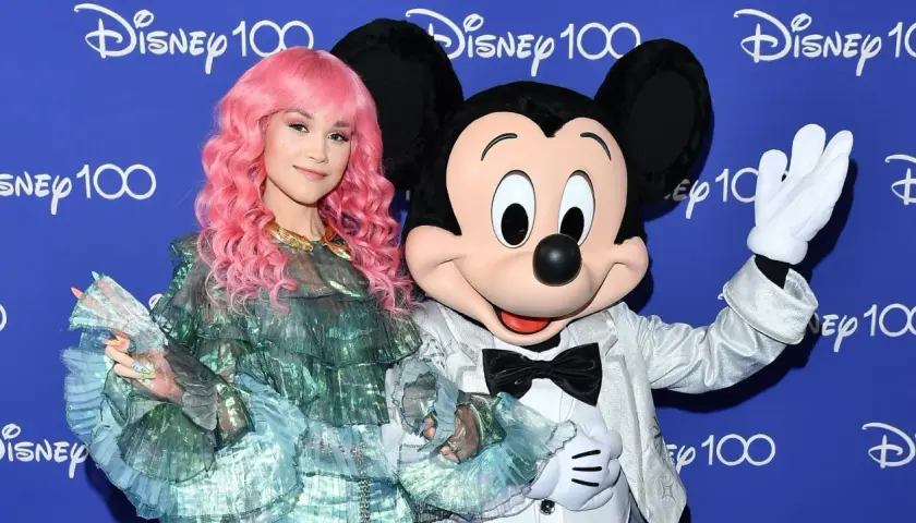 Dziewczyna z różowymi włosami i Myszka Miki pozdrawiają na tle napisu "Disney 100". Może to zapowiedź nowych piosenek Disneya?