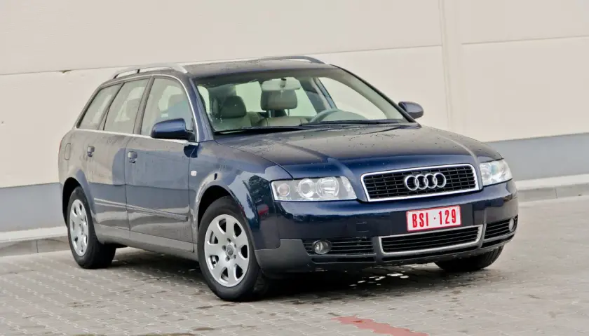 Ciemnoniebieskie Audi A4 B6 Avant na parkingu. Widać przednie reflektory i grill z logo Audi.