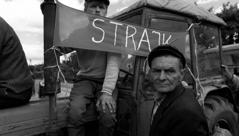 Dwóch mężczyzn w czapkach na tle traktora z banerem "STRAJK".