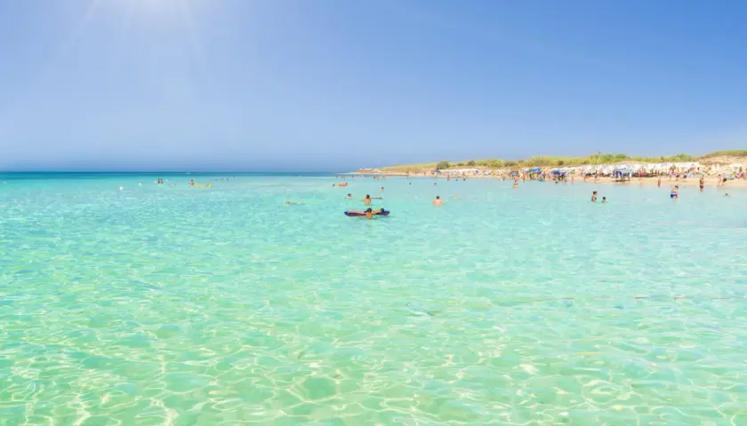 Crystal clear turquoise waters and a sandy beach with sunbathers, perfect for those wondering where to stay in Puglia for beaches.