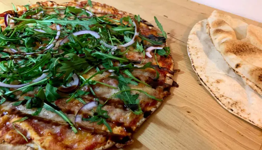 En läcker vegetarisk pizza med ruccola och rödlök, perfekt för dig som söker vegetariska recept. Bredvid ligger nybakade pitabröd.