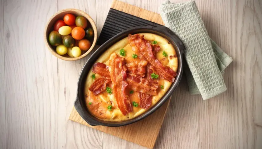 En härlig tjockpannkaka med knaprigt bacon, toppad med persilja. Bredvid en skål med färgglada körsbärstomater.