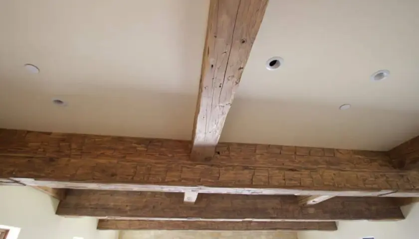 Poutres apparentes en bois ciré, patinées par le temps, soutenant un plafond blanc avec des spots encastrés.