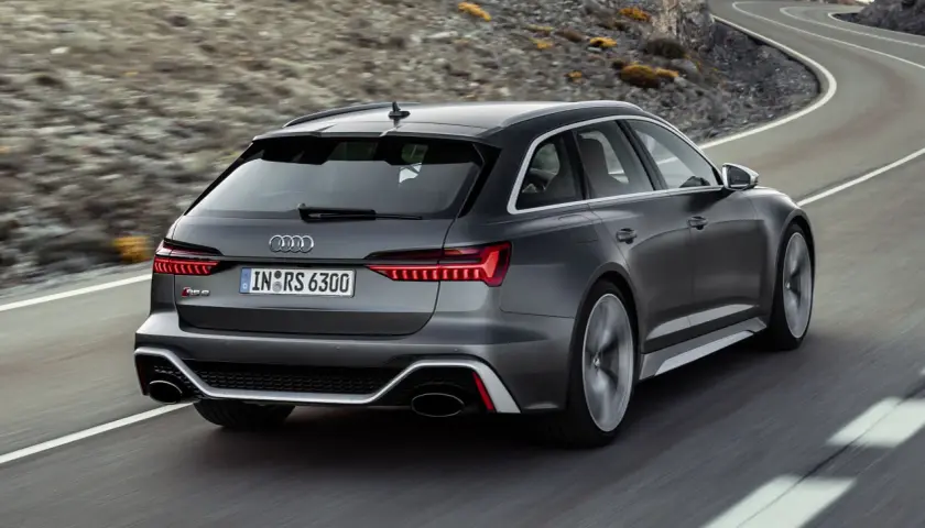 El Audi RS6 ranchera gris oscuro acelera por una carretera sinuosa entre montañas.