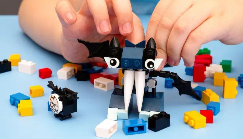 Kinderhände bauen mit bunten Klemmbausteinen einen Fledermaus-Charakter. Ein beliebter Klemmbaustein Hersteller ermöglicht kreativen Spielspaß.