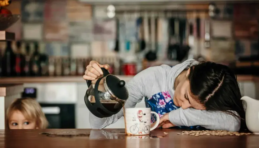 Une femme, visiblement à bout de forces, verse du café dans une tasse, le regard perdu. Un enfant la regarde, l'air intrigué. Elle semble tomber de fatigue.