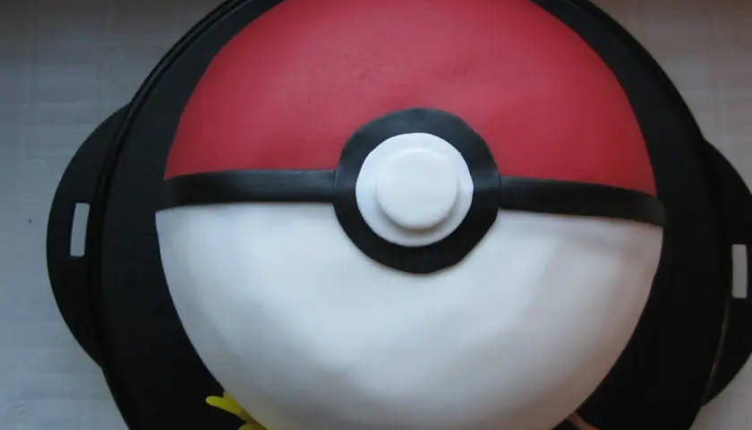 En fantastisk pokemon tårta formad som en pokéboll, med små pokemonfigurer som tittar fram.