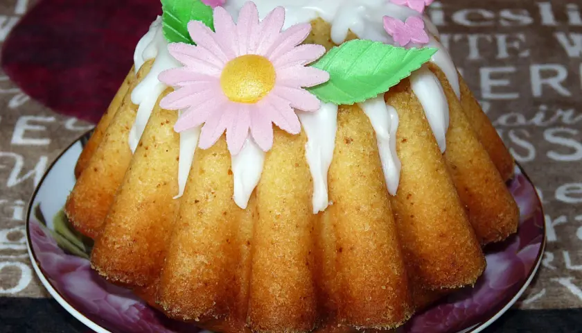 Babka jogurtowa cytrynowa ozdobiona lukrem, różowym kwiatkiem i motylkami. Idealna na wiosenne popołudnie.