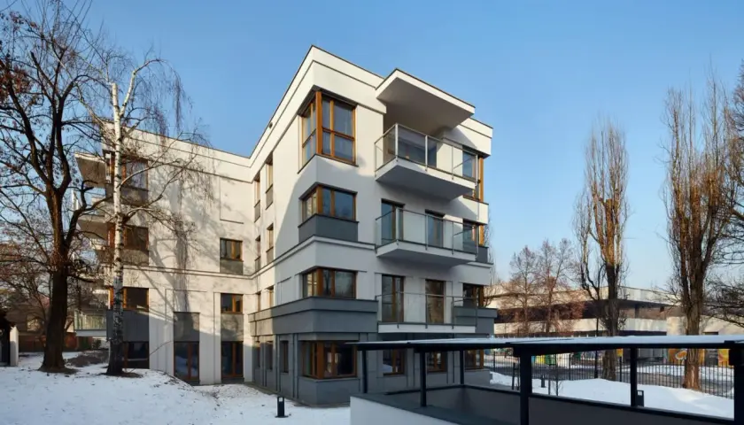 Nowoczesne osiedle oficerskie Kraków, z białymi fasadami i drewnianymi oknami, otoczone zimowym krajobrazem i nagimi drzewami.