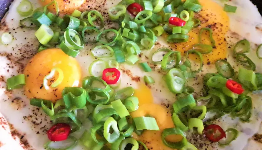 Tortilla z jajkiem, serem i szynką na patelni, posypana szczypiorkiem i papryczką chili.