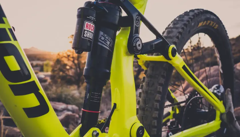 Close-up of a bright yellow mountain bike's rear suspension. The Rock Shox Super Deluxe shock has a length chart visible.