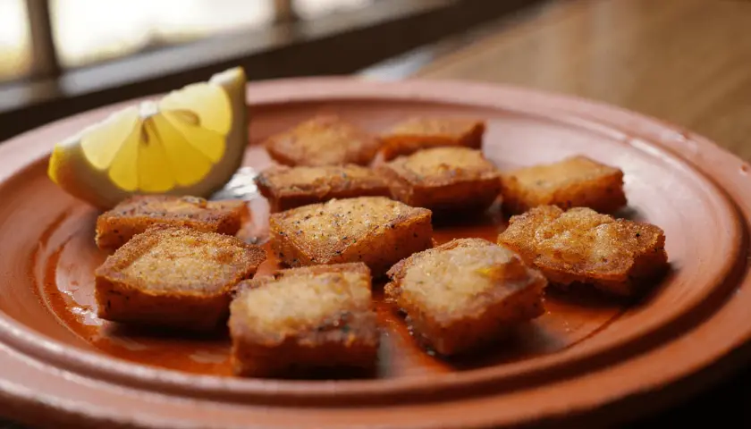 Bocaditos dorados de bacalao rebozado, crujientes y listos para disfrutar, acompañados de una rodaja de limón fresco.